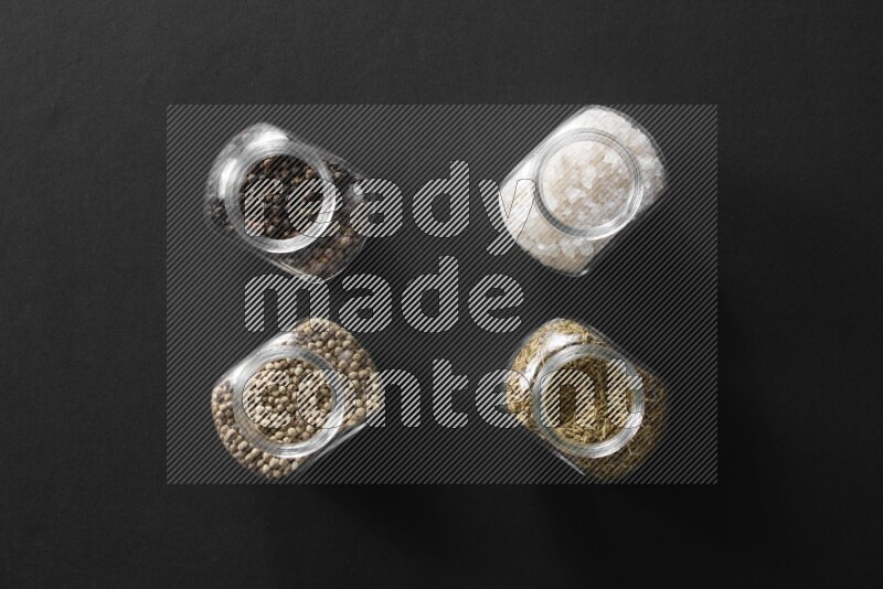 4 glass spice jars full of salt, black peppers, white peppers and cumin on black flooring