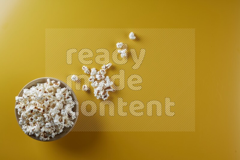A multicolored ceramic plate full of popcorn with popcorn beside it on a yellow background in different angles