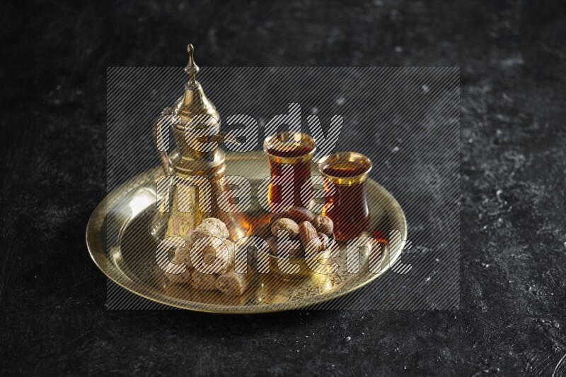 Oriental sweets with dates and a drink on a metal tray in a dark setup
