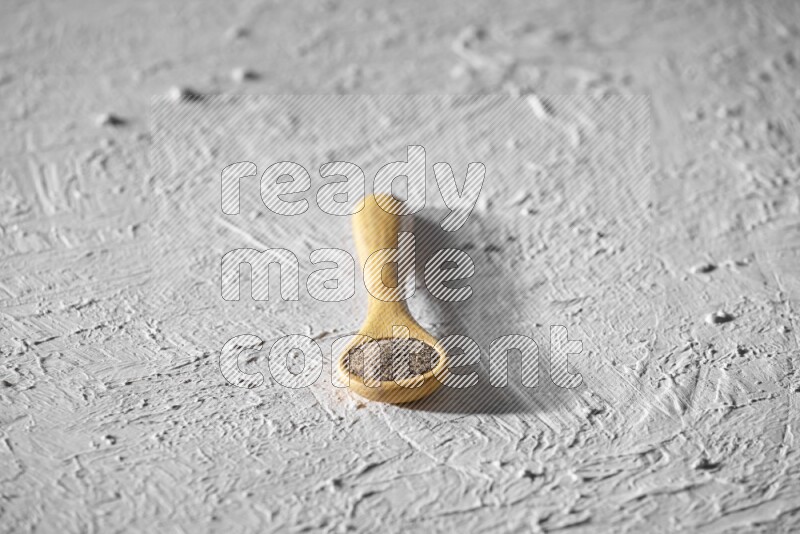 فلفل أسود مطحون في ملعقة خشبية علي خلفية بيضاء