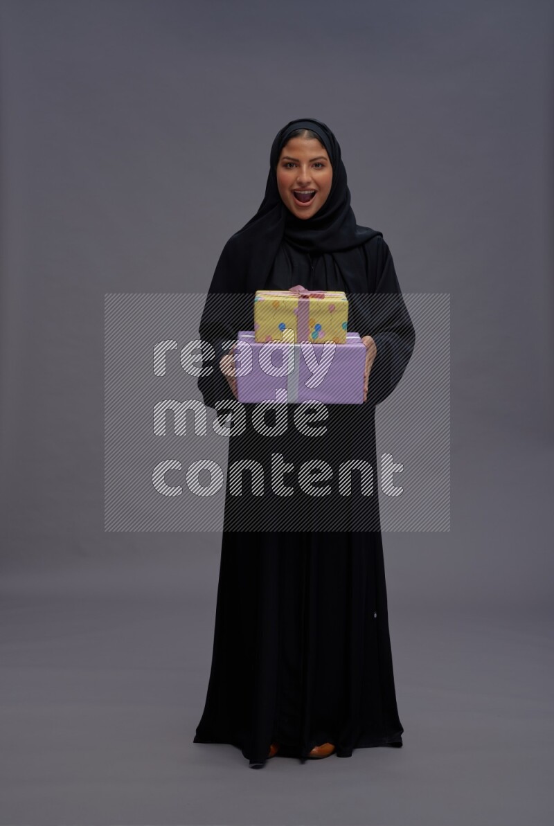 Saudi woman wearing Abaya standing holding gift box on gray background
