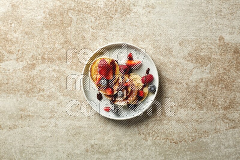 Five stacked mixed berries mini pancakes in a blue plate on beige background