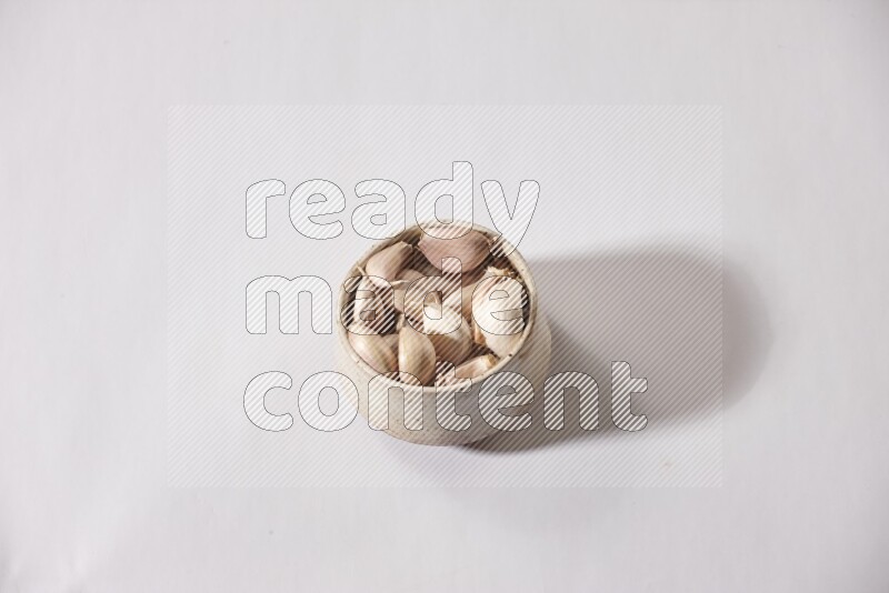 A beige pottery bowl full of garlic cloves on a white flooring