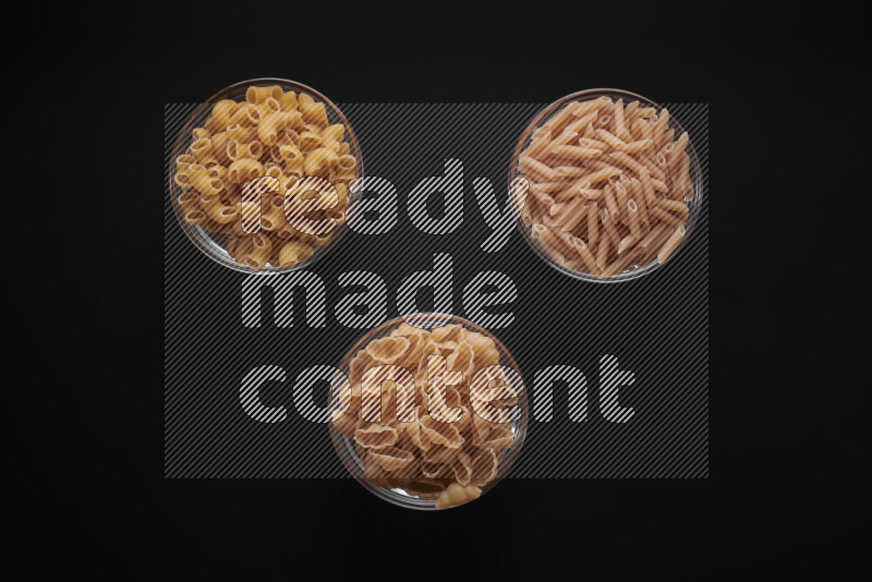 Different pasta types in glass bowls on black background