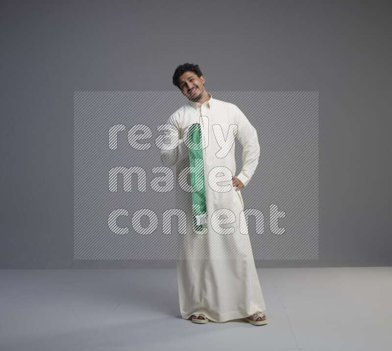 رجل سعودي يرتدي ثوب ابيض ويحمل شال اخضر على خلفية رمادي