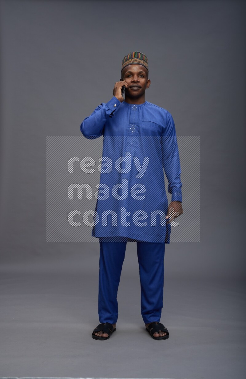 Man wearing Nigerian outfit standing talking on phone on gray background