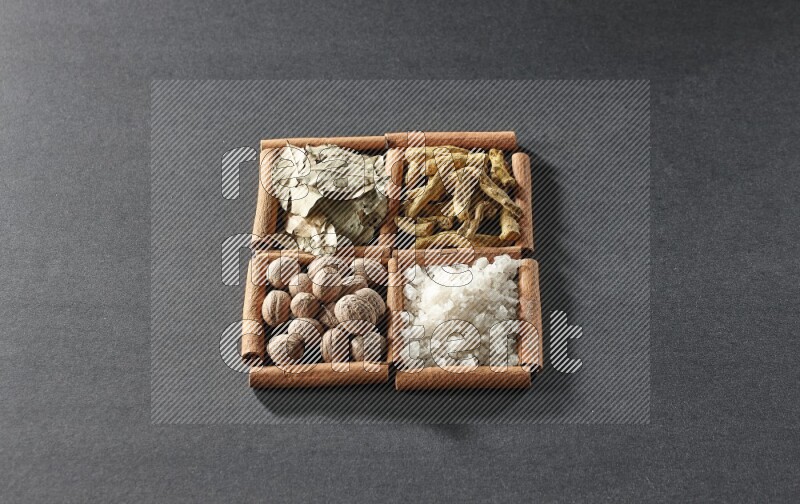 4 مربعات من عيدان القرفة ممتلئة بأوراق الغار والملح الأبيض وأصابع الكركم وجوزة الطيب على أرضية سوداء