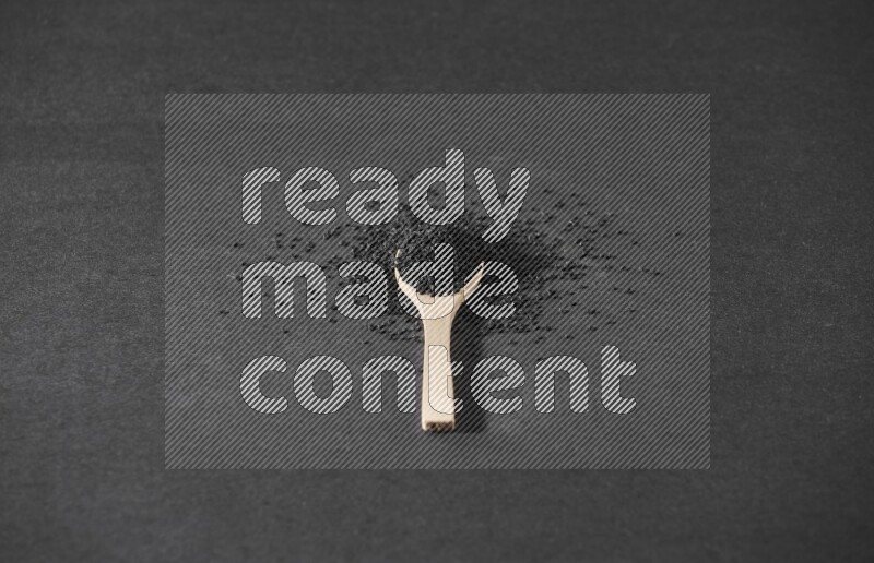 A wooden spoon full of black seeds and surrounded by seeds on a black flooring