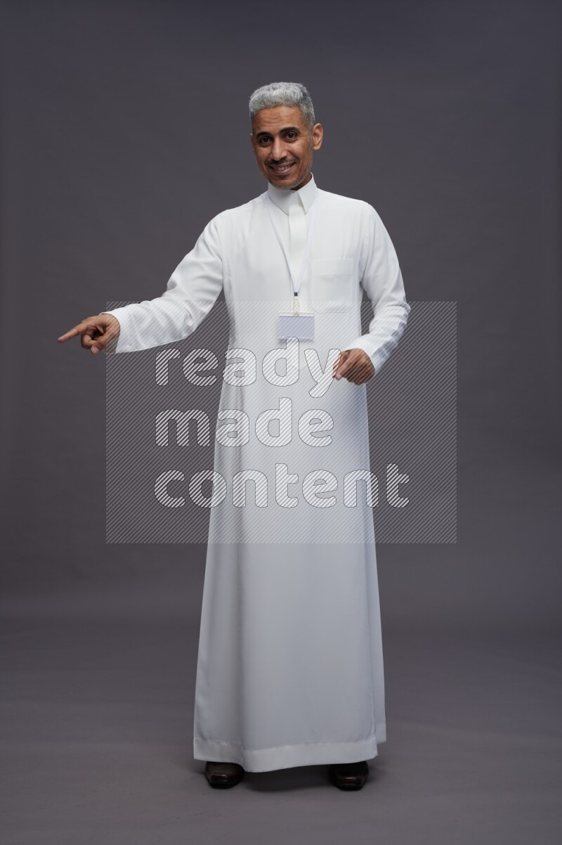 Saudi man wearing thob with neck strap employee badge standing interacting with the camera on gray background