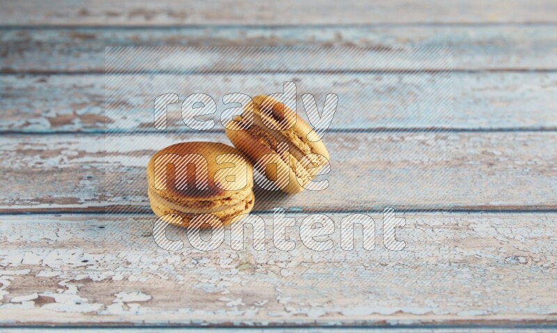 45º Shot of two Yellow Crème Brulée macarons on light blue wooden background