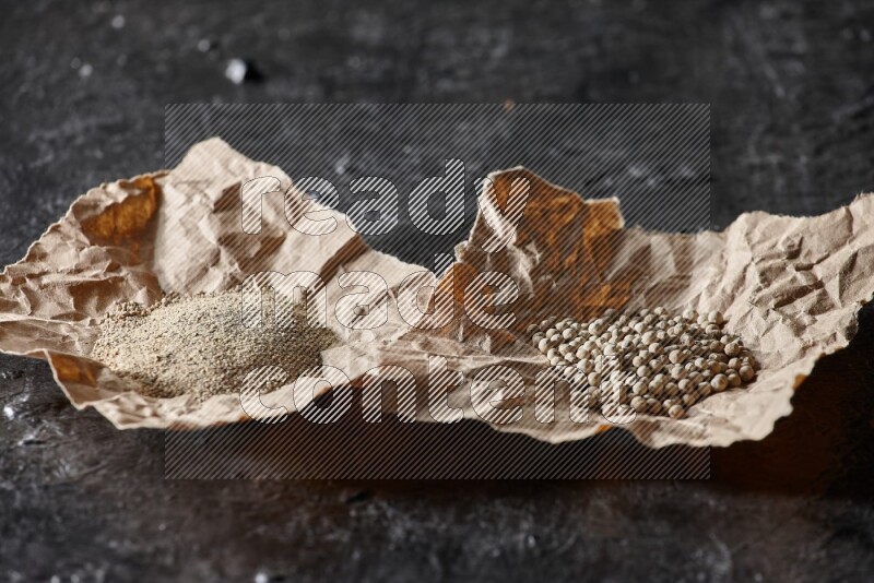 White pepper beads and powder in 2 crumpled paper on textured black flooring
