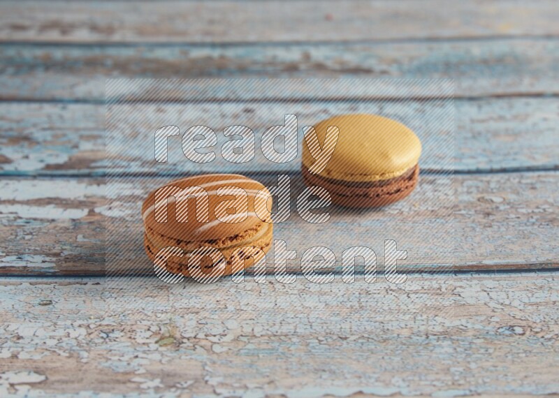 45º Shot of of two assorted Brown Irish Cream, and Yellow, and Brown Chai Latte macarons  on light blue background