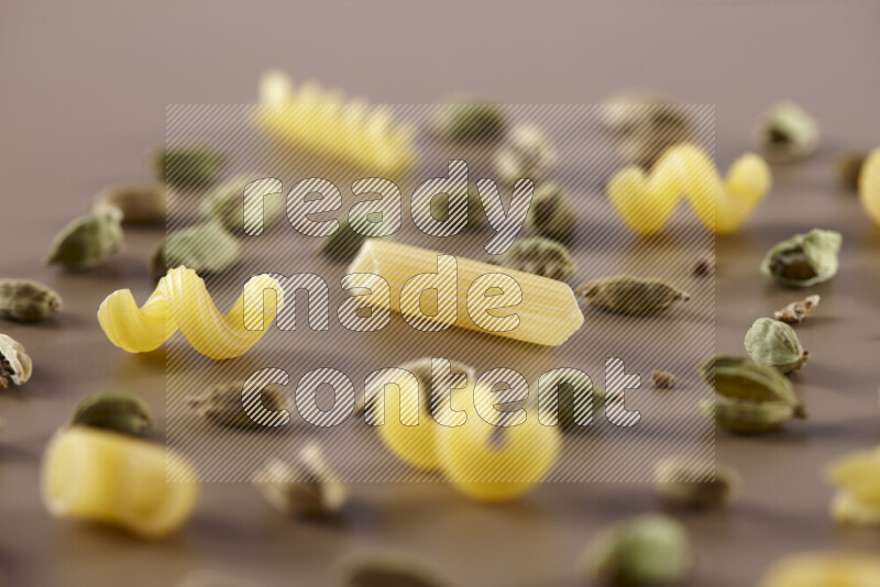 Raw pasta with different ingredients such as cherry tomatoes, garlic, onions, red chilis, black pepper, white pepper, bay laurel leaves, rosemary and cardamom on beige background