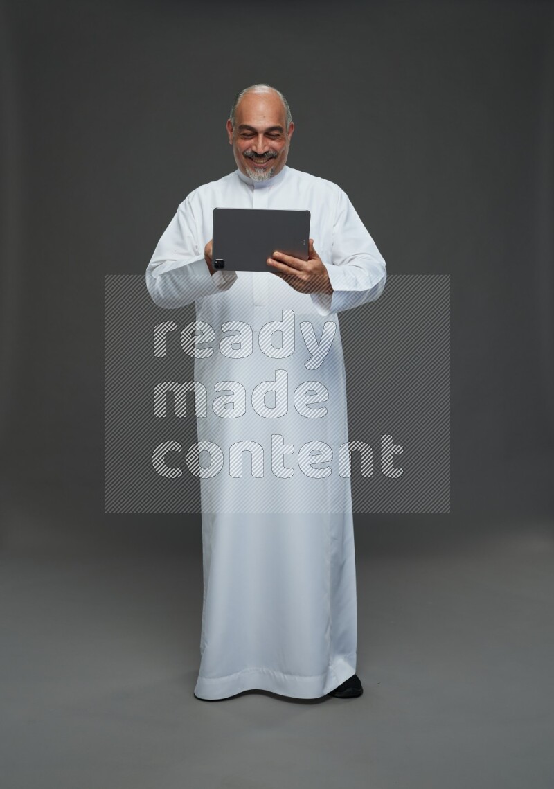 Saudi man without shomag Standing working on tablet on gray background