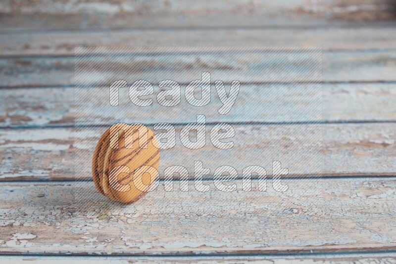 45º Shot of light brown Almond Cream macaron on light blue wooden background