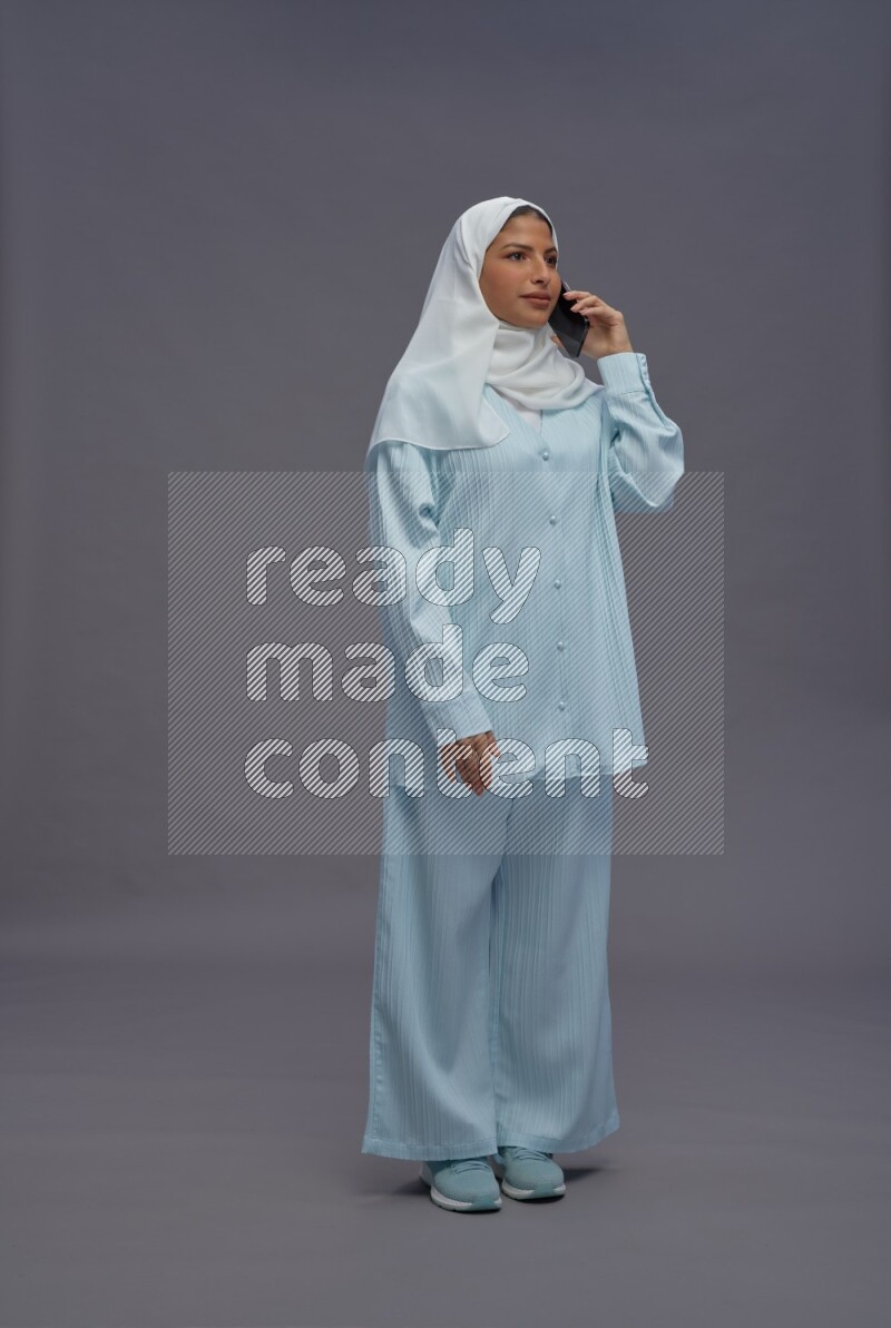 Saudi woman wearing hijab clothes standing talking on phone on gray background