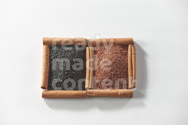 مربعان من أعواد القرفة ممتلئان بحبة البركة السوداء وبذور الكتان علي خلفية بيضاء