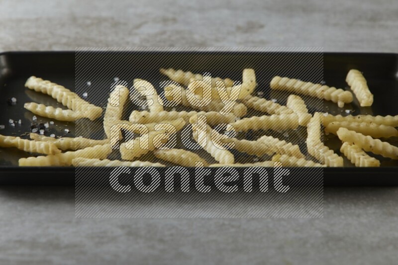 crinkle fries in a black stainless steel rectangle tray on grey textured counter top