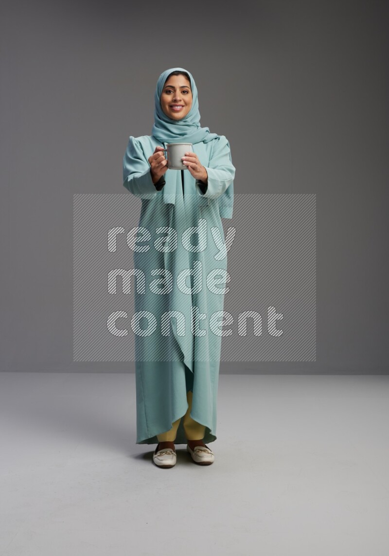 Saudi Woman wearing Abaya standing  holding a mug on Gray background