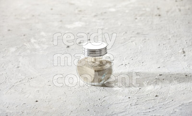 Herbal Glass jar full of white pepper powder on textured white flooring