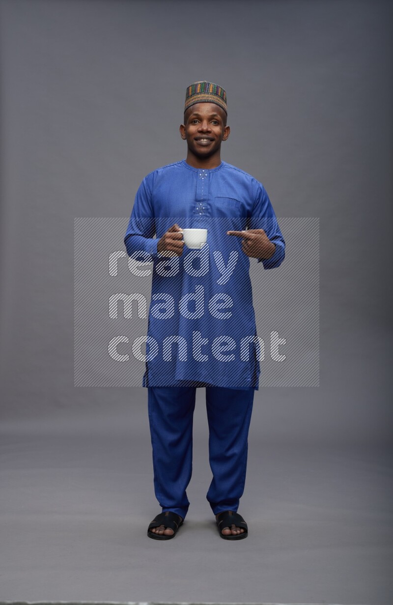 Man wearing Nigerian outfit standing holding mug on gray background