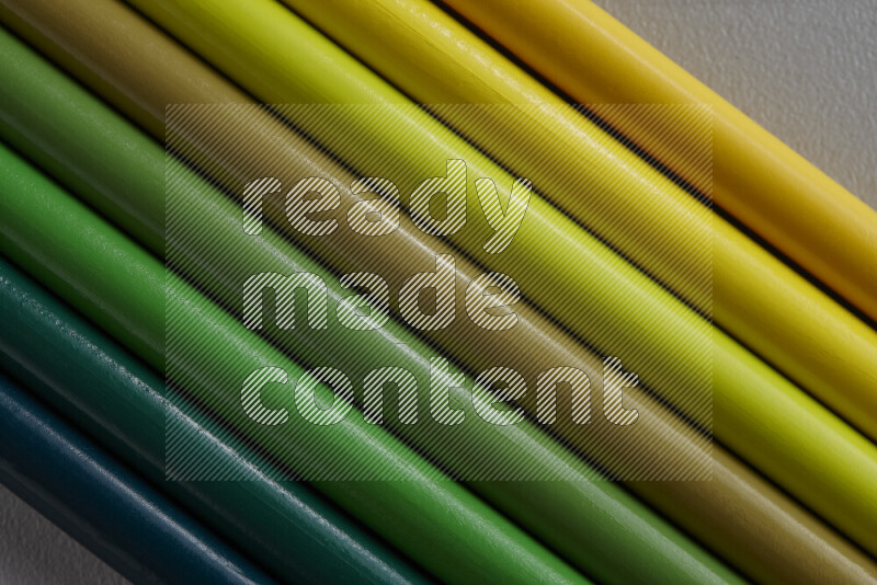 A collection of sharpened colored pencils arranged showcasing a gradient of yellow and green hues on grey background