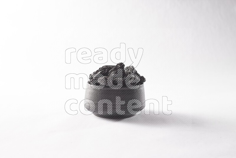 Dried plums in a black pottery bowl on white background