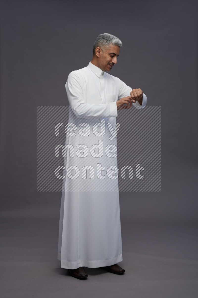 Saudi man wearing thob with neck strap employee badge standing interacting with the camera on gray background
