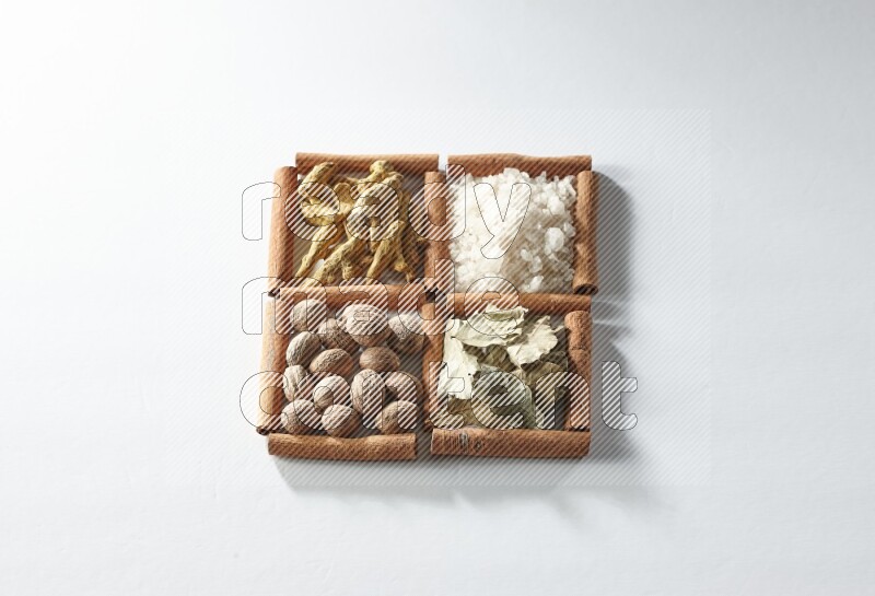 4 مربعات من أعواد القرفة ممتلئة بالملح وورق الغار وجوزة الطيب والكركم على أرضية بيضاء