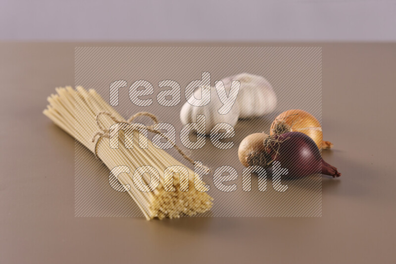 Raw pasta with different ingredients such as cherry tomatoes, garlic, onions, red chilis, black pepper, white pepper, bay laurel leaves, rosemary and cardamom on beige background