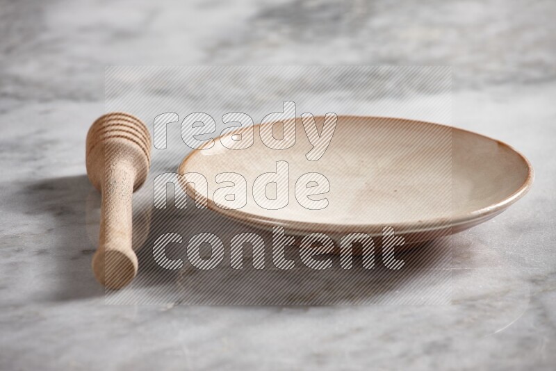 Beige pottery plate with wooden honey dipper on the side on grey marble background