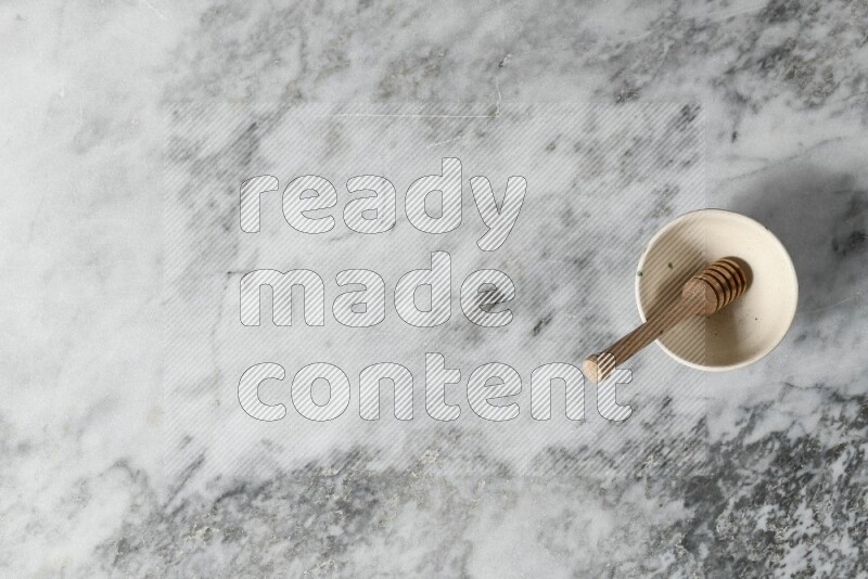 Beige pottery bowl with wooden honey dipper in it on grey marble background