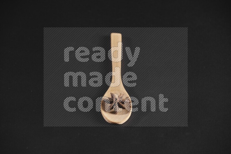 اليانسون النجمي في ملعقة خشبية فوق اليانسون النجمي الذي يغطي الإطار على أرضية سوداء