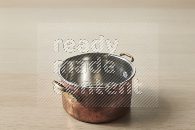A small copper pot on light wooden background