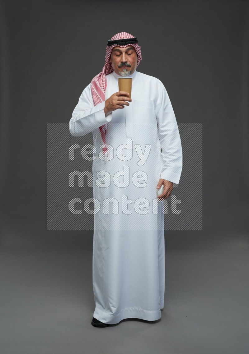 Saudi man with shomag Standing holding paper cup on gray background