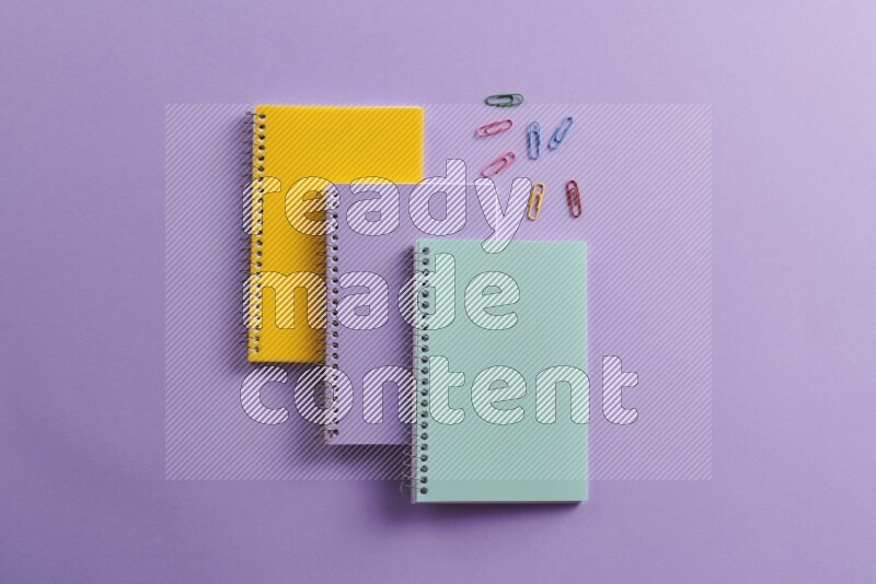 Multicolored notebooks with different school supplies on purple background