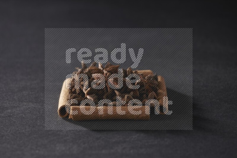 A single square of cinnamon sticks full of star anise on black flooring