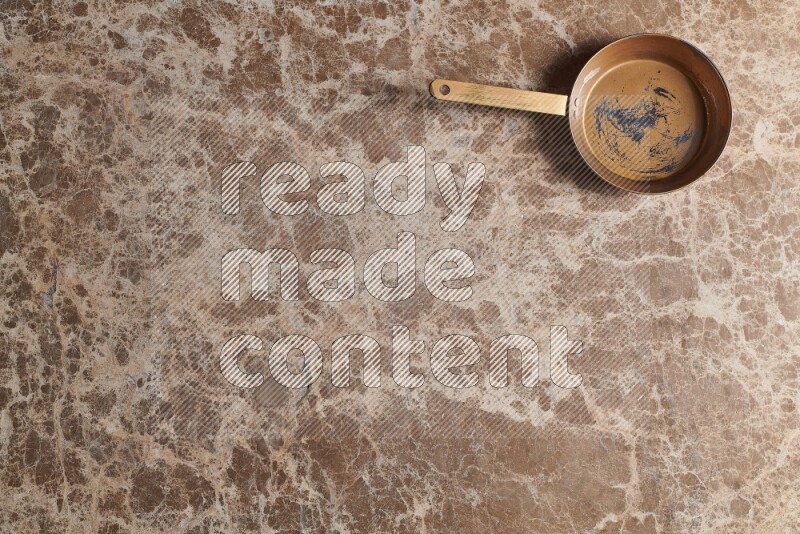 A small copper pan on beige marble background