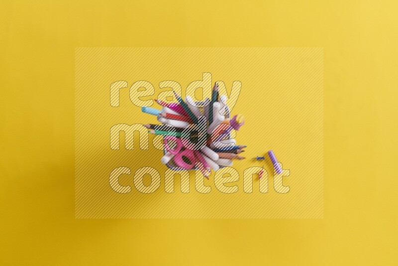 Pens, pencils and school supplies in a metal pen holder on yellow background