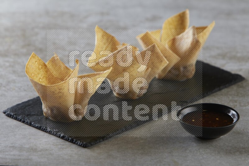 wonton cups with soy sauce ramkin on rectangle slate on grey textured counter top