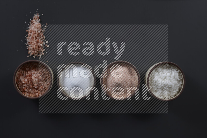 4 وعاء فخاري ممتلئين بملح الهيمالايا والملح الأبيض على خلفية سوداء