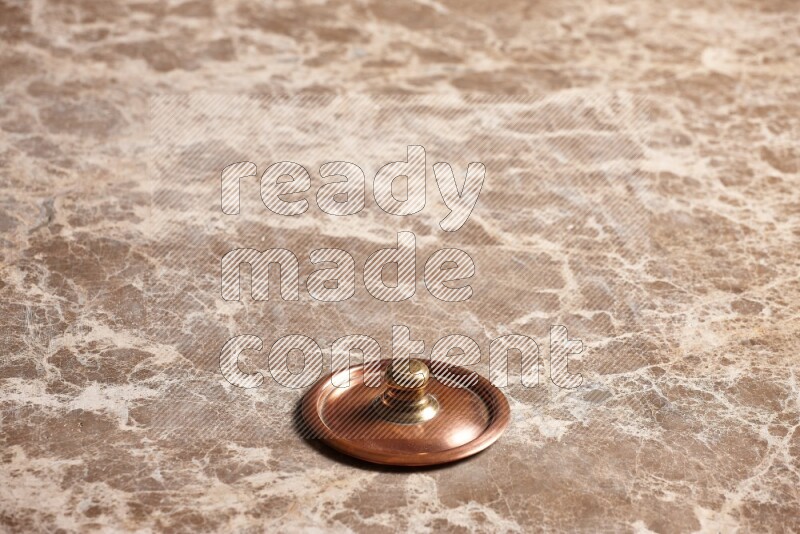 A small copper pot lid on beige marble background