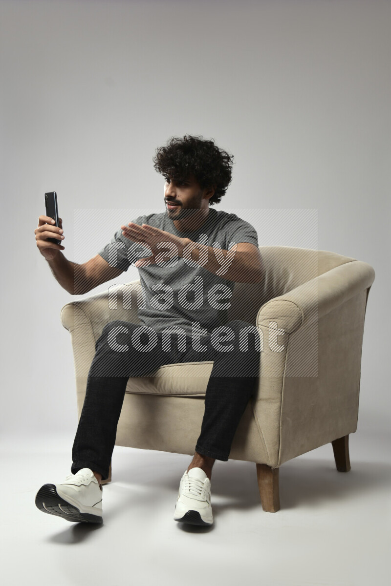 A man wearing casual sitting on a chair shooting with his phone on white background
