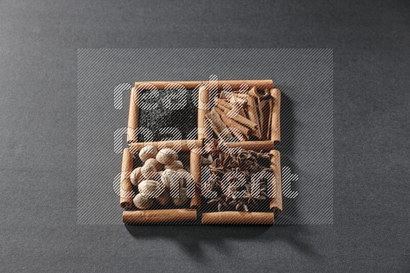 4 squares of cinnamon sticks full of black seeds, cinnamon, star anise and nutmegs on black flooring