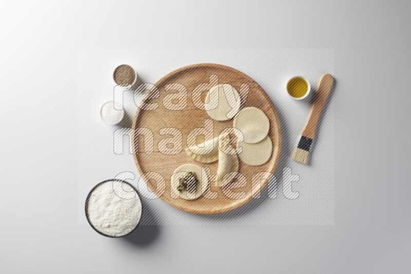 two closed sambosas and one open sambosa filled with meat while flour, salt, black pepper and oil with oil brush aside in a wooden dish on a white background