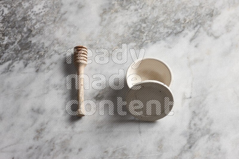 White pottery bowl with wooden honey dipper on the side on grey marble background