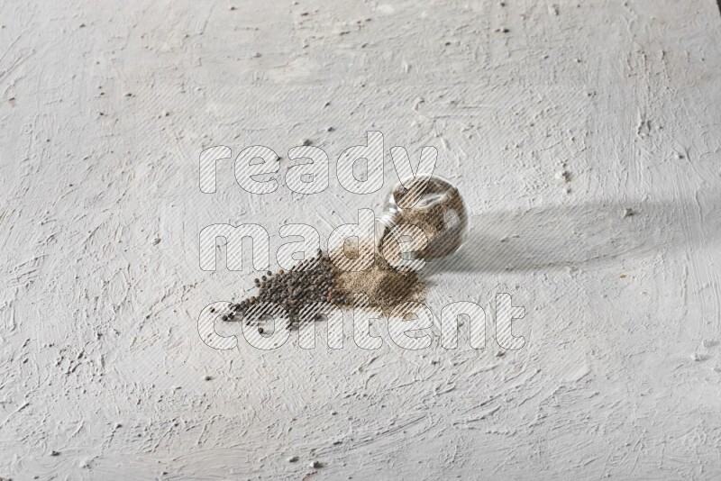 Flipped glass spice jar full of black pepper powder and paper beads beside it on a textured white flooring