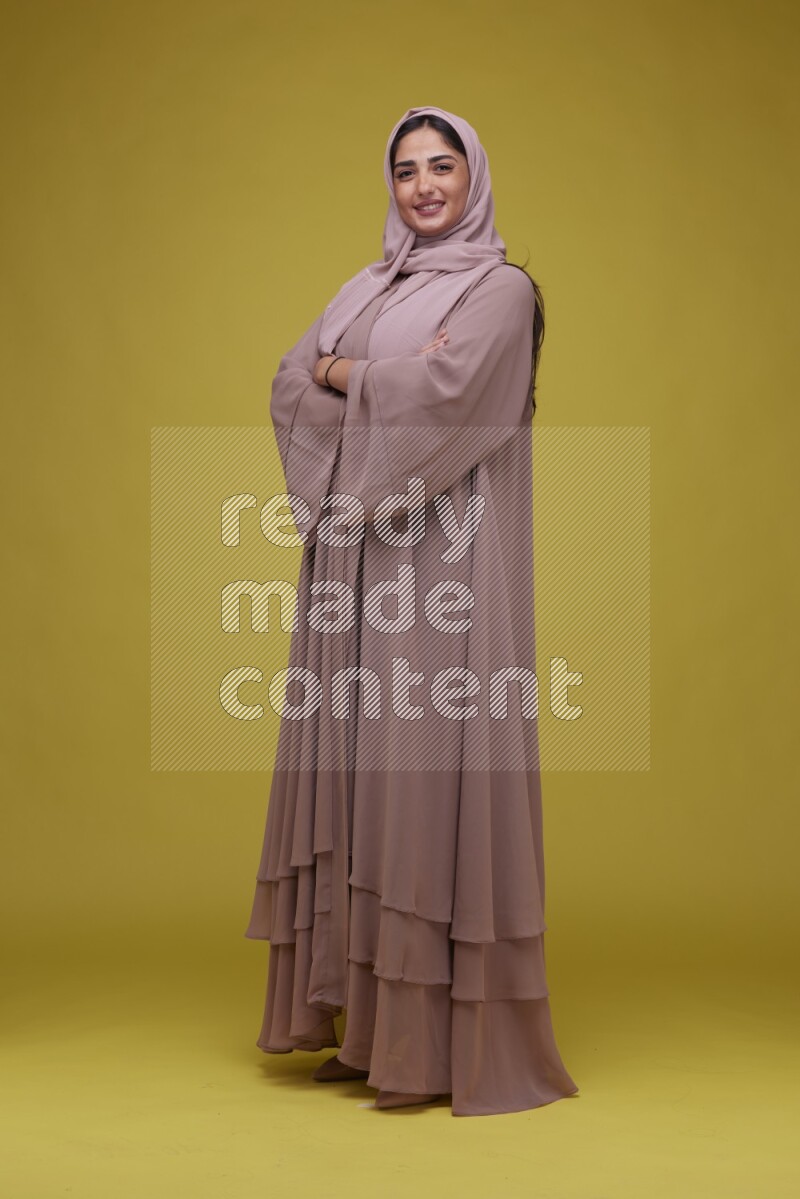 A woman Posing on a Yellow Background wearing Brown Abaya with Hijab