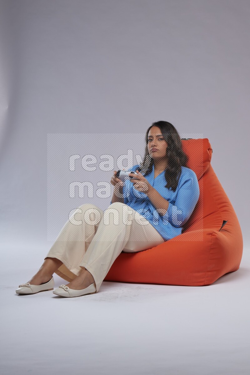 A woman sitting on an orange beanbag and gaming with joystick