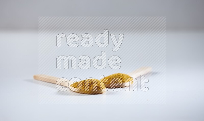 2 wooden spoons full of turmeric powder on white flooring